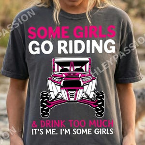 以下が含まれることがあります： ピンクと白で「SOME GIRLS GO RIDING」と書かれた濃い灰色のTシャツ。その下にピンクと白のオフロード車のグラフィックがあります。「& DRINK TOO MUCH IT'S ME. I'M SOME GIRLS」というテキストがその下に印刷されています。
