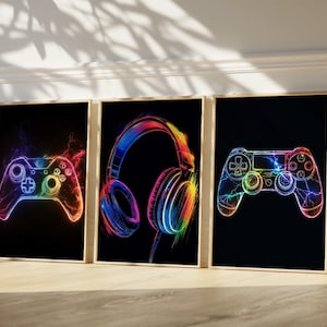 May include: Three framed art prints with neon illustrations of gaming accessories. The prints depict a controller, headphones, and another controller, all in vibrant rainbow colours against a black backdrop. The artwork has a modern, digital art aesthetic.