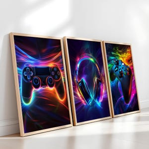 May include: Three framed art prints with gaming themes. The prints depict a black game controller, headphones, and another controller, all with vibrant neon light effects against a dark background. The frames are a light wood colour.