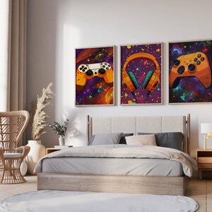 May include: Three framed art prints depicting gaming controllers and headphones set against a colourful space-themed backdrop. The artwork uses shades of orange, purple, and green, adding a vibrant touch to the bedroom decor. The prints are displayed above a bed.