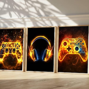 May include: Set of three framed art prints featuring gaming-themed designs. Each print showcases a different element: a controller, headphones, and another controller, all rendered with fiery orange and yellow hues against a black background.