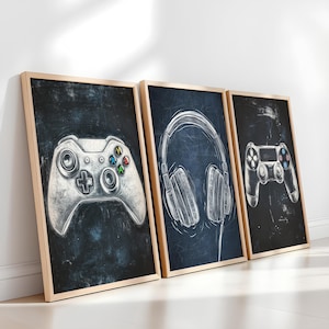 May include: Three framed art prints featuring gaming-themed illustrations. The prints showcase a game controller, headphones, and another game controller, all rendered in a sketch-like style with a white outline against a dark blue background. The frames are light brown.