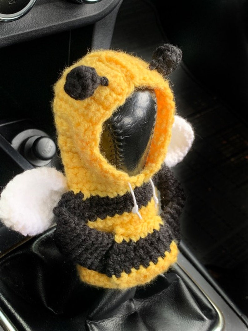 Puede incluir: Una funda de palanca de cambios de ganchillo con forma de abeja, con un cuerpo a rayas amarillo y negro, alas blancas y antenas negras. La funda est&aacute; dise&ntilde;ada para adaptarse a una palanca de cambios est&aacute;ndar.
