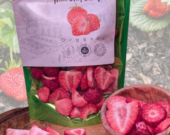 May include: A package of freeze-dried strawberries with the text "Nature in its purest form". The package is green and white, with a drawing of strawberries. Sliced strawberries are in a wooden bowl and scattered on a wooden surface. The product is labeled organic, gluten-free, and non-GMO.