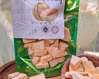 May include: A shiny green stand-up pouch containing freeze-dried cantaloupe pieces. The label features the text "Nature in its purest form Freeze Dried Cantaloupe" and "Organic" with icons for gluten-free, non-GMO, and no added sugar certifications.