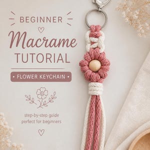 Könnte beinhalten: Ein Makramee-Blumen-Schlüsselanhänger in Rosa und Weiß mit einer Holzperle in der Mitte. Der Schlüsselanhänger hat einen silbernen herzförmigen Verschluss. Das Bild ist Teil eines Anfänger-Makramee-Tutorials. Der Text lautet "BEGINNER Macrame TUTORIAL" und "FLOWER KEYCHAIN."