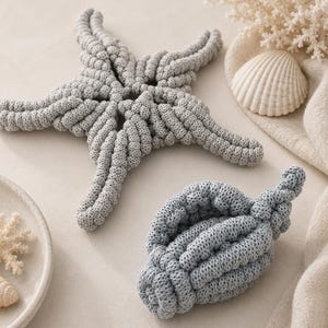 May include: A light gray crocheted starfish and a matching light gray crocheted seashell. Both items feature a thick, textured corded knit pattern. The starfish has five distinct arms, while the seashell has a spiral, ribbed structure.