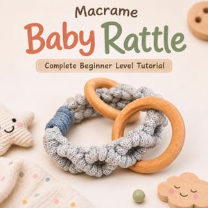 May include: A macrame baby rattle featuring two smooth wooden rings intertwined with light gray knotted cord and a blue accent section. The text Macrame Baby Rattle Complete Beginner Level Tutorial is visible above the rattle, alongside a small crocheted star and a wooden cloud shape.