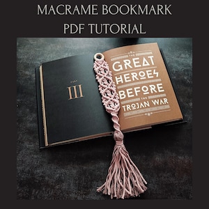 Puede incluir: Un marcapáginas de macramé rosa claro con borla, sobre un libro abierto. El marcapáginas tiene un diseño tejido. El libro muestra el texto "THE GREAT HEROES BEFORE THE TROJAN WAR". La imagen también incluye el texto "MACRAME BOOKMARK PDF TUTORIAL".