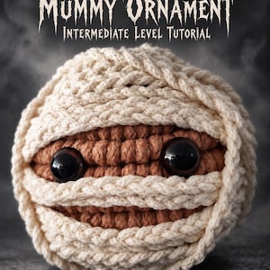 May include: A round macrame mummy ornament featuring cream-colored cord wrapped around a brown base with two large, glossy black eyes. The text above reads 3D MACRAME MUMMY ORNAMENT INTERMEDIATE LEVEL TUTORIAL.