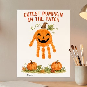 May include: A white rectangular art print featuring the orange text CUTEST PUMPKIN IN THE PATCH. In the center is an orange handprint shaped like a jack-o'-lantern with a black face. Below are two orange pumpkins with green leaves and a Name line.