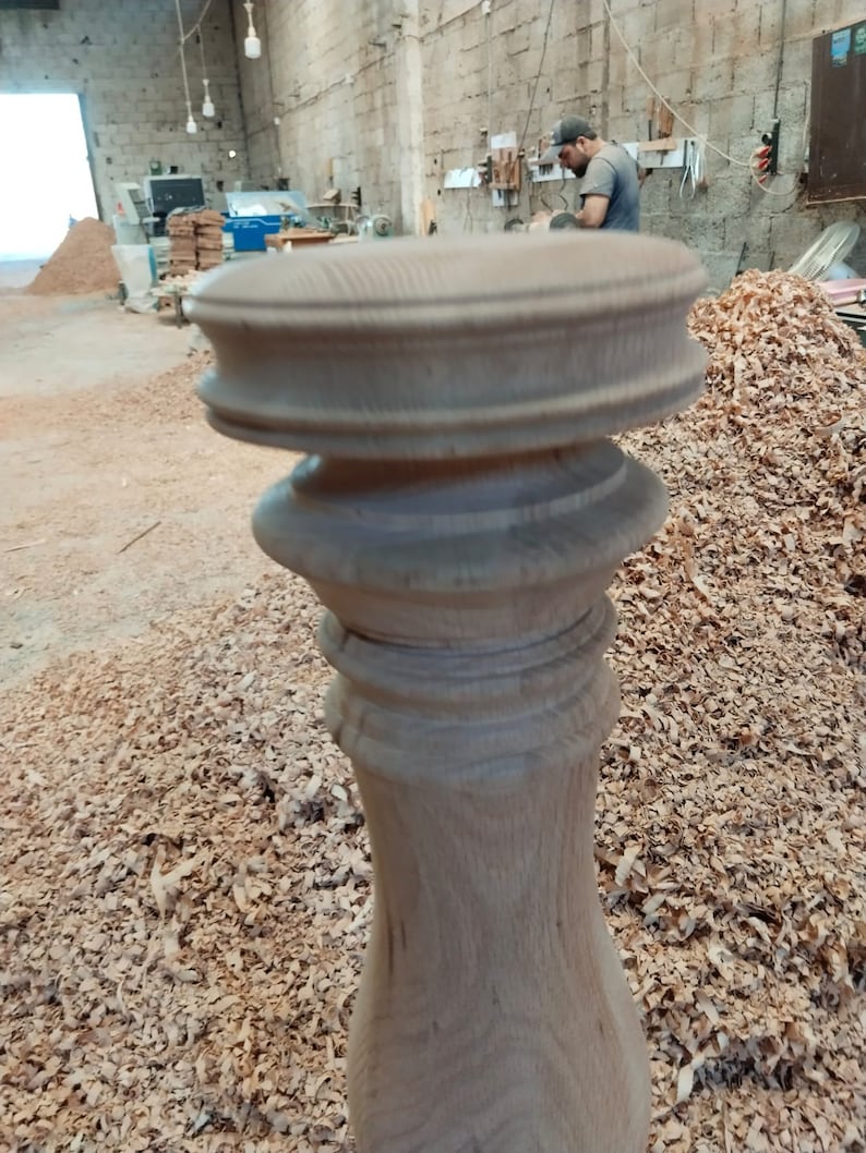 Puede incluir: Primer plano de una pata de mesa de madera con tallas intrincadas. La pata est&aacute; hecha de madera marr&oacute;n claro y tiene un acabado liso y pulido. La pata est&aacute; rodeada de virutas de madera.
