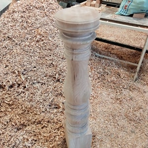 Puede incluir: Primer plano de una pata de mesa de madera con un dise&ntilde;o torneado. La pata est&aacute; sin terminar y tiene una base cuadrada. La pata est&aacute; rodeada de virutas de madera.