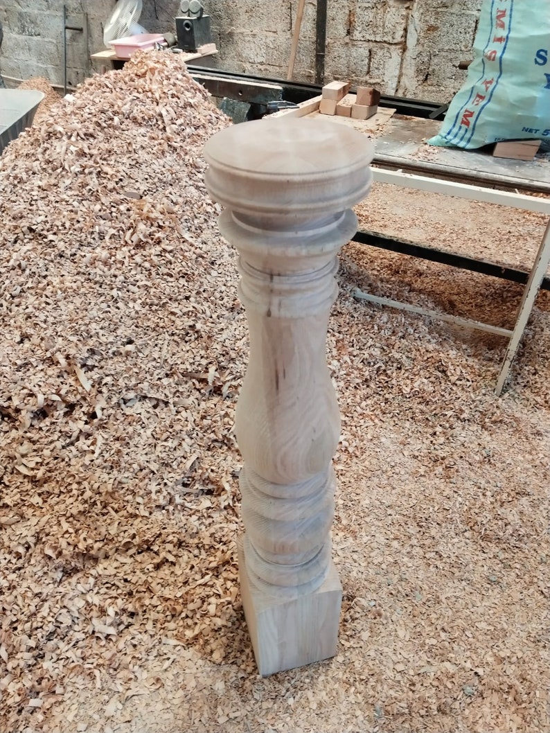 Puede incluir: Primer plano de una pata de mesa de madera con un dise&ntilde;o torneado. La pata est&aacute; sin terminar y tiene una base cuadrada. La pata est&aacute; rodeada de virutas de madera.