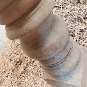 Puede incluir: Primer plano de una pata de mesa de madera con un dise&ntilde;o torneado. La pata est&aacute; hecha de madera de color claro y tiene un acabado liso y pulido.