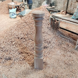 Puede incluir: Primer plano de una pata de mesa de madera con un dise&ntilde;o torneado. La pata est&aacute; sin terminar y tiene un color de madera natural. La pata est&aacute; rodeada de virutas de madera.