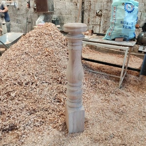Puede incluir: Un balaustre de madera con una base cuadrada y una parte superior torneada. El balaustre est&aacute; rodeado de virutas de madera.