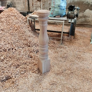 Puede incluir: Primer plano de una pata de mesa de madera con un dise&ntilde;o torneado. La pata est&aacute; hecha de madera de color claro y tiene una base cuadrada. La pata est&aacute; rodeada de virutas de madera.