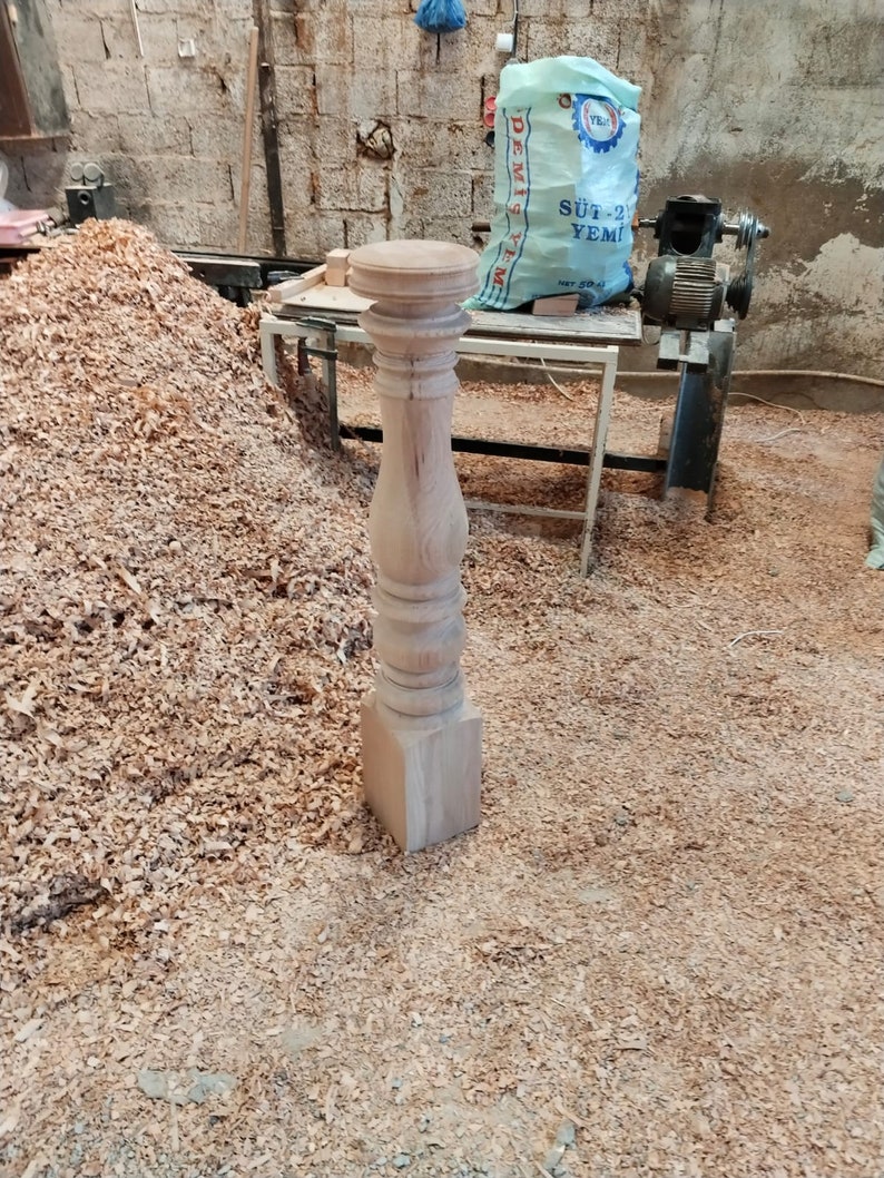 Puede incluir: Primer plano de una pata de mesa de madera con un dise&ntilde;o torneado. La pata est&aacute; hecha de madera de color claro y tiene una base cuadrada. La pata est&aacute; rodeada de virutas de madera.