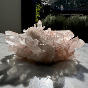 Könnte beinhalten: Ein großer Cluster aus rosafarbenen Quarzkristallen mit verschiedenen Formen und Größen. Die Kristalle sind in einem Cluster angeordnet, wobei einige der Kristalle nach oben und andere nach unten zeigen. Die Kristalle sind durchscheinend und haben einen leichten rosa Farbton.