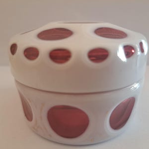 Peut inclure: Un récipient rond blanc avec couvercle et des accents circulaires rouges. Le récipient a une finition brillante et un design décoratif. Le couvercle et le corps sont de la même taille. Le récipient est probablement en verre.