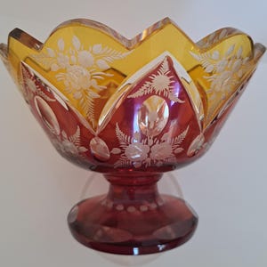 May include: A red and amber glass bowl with a footed base. The bowl is decorated with etched floral designs.