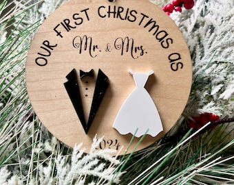 May include: A round wooden bauble with the text "Our First Christmas as Mr. & Mrs. 2024" and a black tuxedo and white dress cutout.
