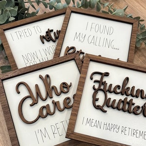May include: Four wooden signs with white backgrounds and black text. The signs have different sayings about retirement. The first sign says "I tried to return now I work for my retirement". The second sign says "I found my calling... retirement". The third sign says "Who cares I'm retired". The fourth sign says "Fuckin Quitter I mean happy retirement".