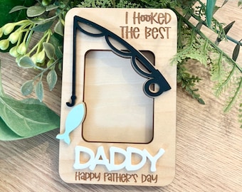 Könnte beinhalten: Holzbildrahmen mit einem Angelruten-Design. Der Rahmen hat einen Ausschnitt für ein Foto und den Text "Ich habe den besten Papa gefangen Frohes Vatertags".