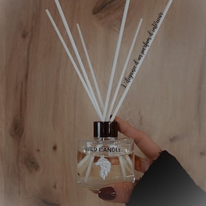 Peut inclure: Un diffuseur en verre transparent avec des bâtonnets blancs et un bouchon marron foncé. Le flacon porte l'inscription "WILD CANDLE" et un logo de tête de loup. Le texte "L'élégance d'un parfum d'intérieur" est également présent.
