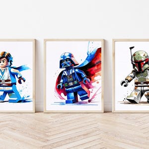 May include: Three framed watercolor prints featuring Star Wars characters in Lego form. The prints depict Luke Skywalker with a blue lightsaber, Darth Vader with a red and blue cape, and Boba Fett in his iconic armor. The artwork has a watercolor effect.