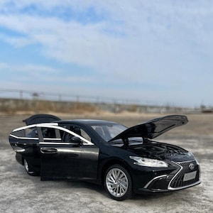 May include: A black model car with the hood and doors open, revealing the engine and interior. The car has silver rims and is set against a cloudy sky.
