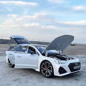 May include: A white Audi RS7 Sportback model car with the bonnet, doors, and boot open. The car has black rims with red brake calipers. The front grill has the Audi logo and the text "RS7 Sportback".