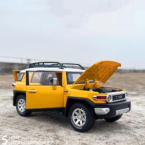 May include: A yellow and white Toyota FJ Cruiser model with the hood open and the door ajar. The model is 8.5 inches long, 3.5 inches wide, and 3.8 inches tall. The model has black tires and a black roof rack.