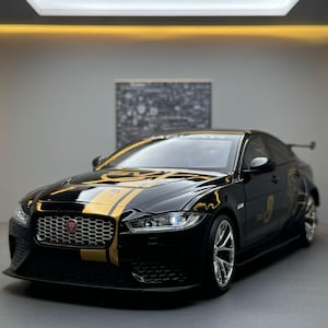 Könnte beinhalten: Schwarzes Jaguar-Modellauto mit goldenen Rennstreifen und der Nummer 9 an der Seite. Das Auto hat einen Spoiler und Chromfelgen. Das Jaguar-Logo ist auf dem Kühlergrill sichtbar.