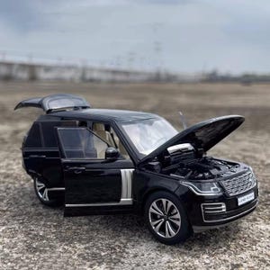 Puede incluir: Modelo de SUV Land Rover negro con capó y puertas abiertas, mostrando el motor y el interior. El modelo tiene detalles plateados y ruedas detalladas, sobre un fondo exterior neutro.