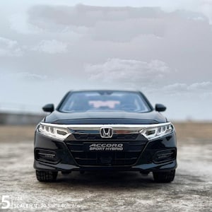 Può includere: Un'auto modello nera Honda Accord Sport Hybrid. La parte anteriore dell'auto è visibile, mostrando i fari, la griglia e il testo "ACCORD SPORT HYBRID". Il modello è lungo 20,5 cm, largo 8,6 cm e alto 6 cm.