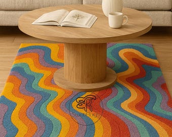 May include: A colorful, wavy-patterned rug in shades of orange, yellow, blue, and purple. The rug is placed under a wooden coffee table with a book, a mug, and a vase of yellow flowers. The rug has the text "Sweet Rugs".