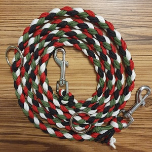 Puede incluir: Correa trenzada para perros en espiral. La correa presenta una combinación de hebras rojas, negras, blancas y verdes. Tiene dos cierres metálicos y un anillo metálico para sujetar al collar o arnés.