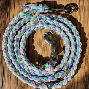 Puede incluir: Una correa de perro trenzada en tonos lavanda, verde menta y blanco con cierres de metal plateado y un anillo.