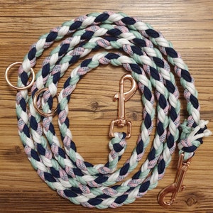 Puede incluir: Una correa de perro trenzada con un clip de oro rosa y dos anillos de oro rosa. La correa está hecha de cuerda blanca, rosa, azul y verde.