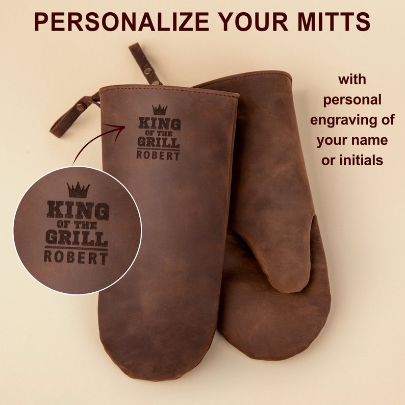 May include: A pair of brown leather oven mitts with the text "King of the Grill" and a crown design, personalized with the name "Robert".