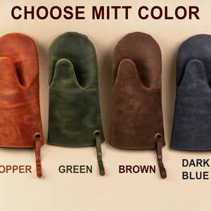 May include: Four leather oven mitts in different colors: copper, green, brown, and dark blue. The mitts have a hanging loop and the colors are labeled below each mitt.