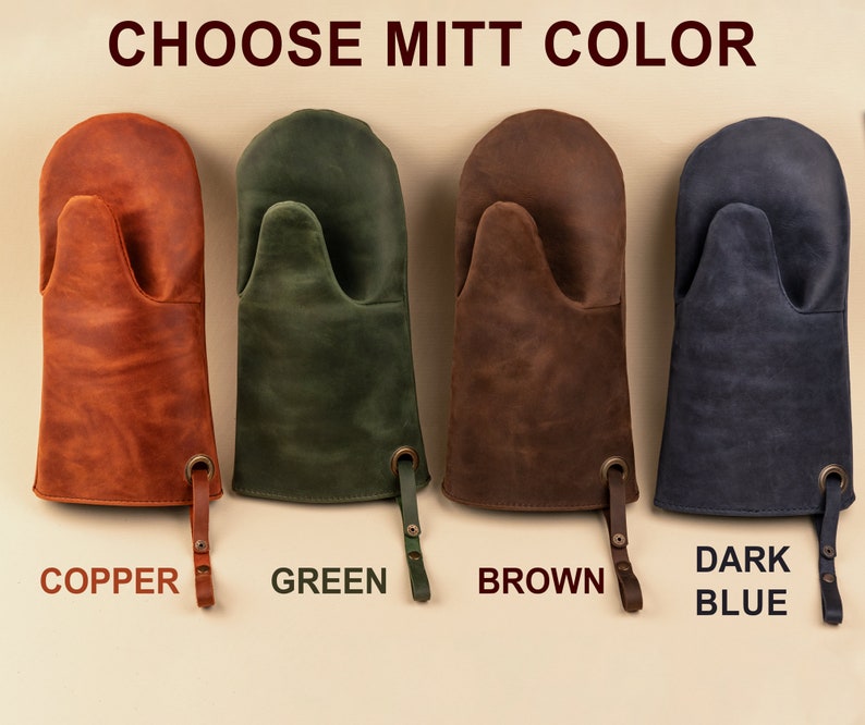 May include: Four leather oven mitts in different colors: copper, green, brown, and dark blue. The mitts have a hanging loop and the colors are labeled below each mitt.