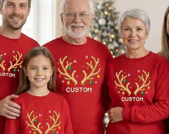 May include: A group of matching red crewneck sweatshirts featuring a graphic of gold reindeer antlers decorated with small colorful ornaments and the word CUSTOM printed in white text below the antlers on the front of each garment.