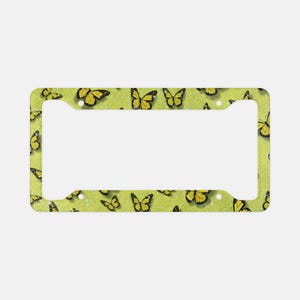 May include: A rectangular license plate frame featuring a bright lime green background with a glittery texture. The frame is decorated with numerous yellow butterflies with black wing details scattered across the entire surface area.
