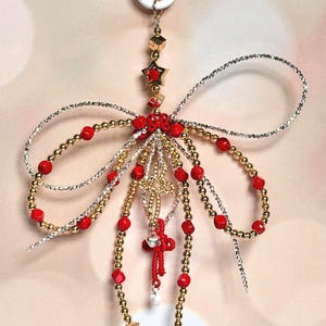 Peut inclure: Un ornement décoratif suspendu composé d'un nœud central orné de perles rouges et dorées. Il comprend des fils métalliques dorés et argentés, des perles rouges sphériques, une étoile dorée, un petit papillon rouge et un cœur argenté.