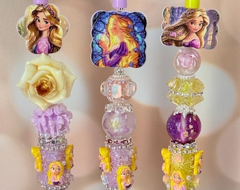May include: Three decorative pens featuring princess-themed designs. Each pen has a different color scheme, including purple, yellow, and green. The pens are adorned with beads, rhinestones, and princess character images.