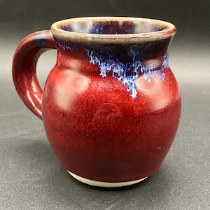May include: A red ceramic mug with a blue glaze on the rim. The mug has a rounded body and a handle.