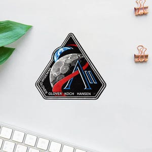 Op de afbeelding: Een witte keramische mok met een zwarte handgreep en de tekst "But First, Coffee" in een vetgedrukte, zwarte letter. De mok staat tegen een vage achtergrond, wat een gezellige setting suggereert.